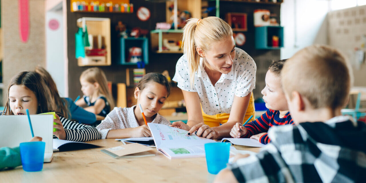 Group of children in classroom studying with woman teacher.